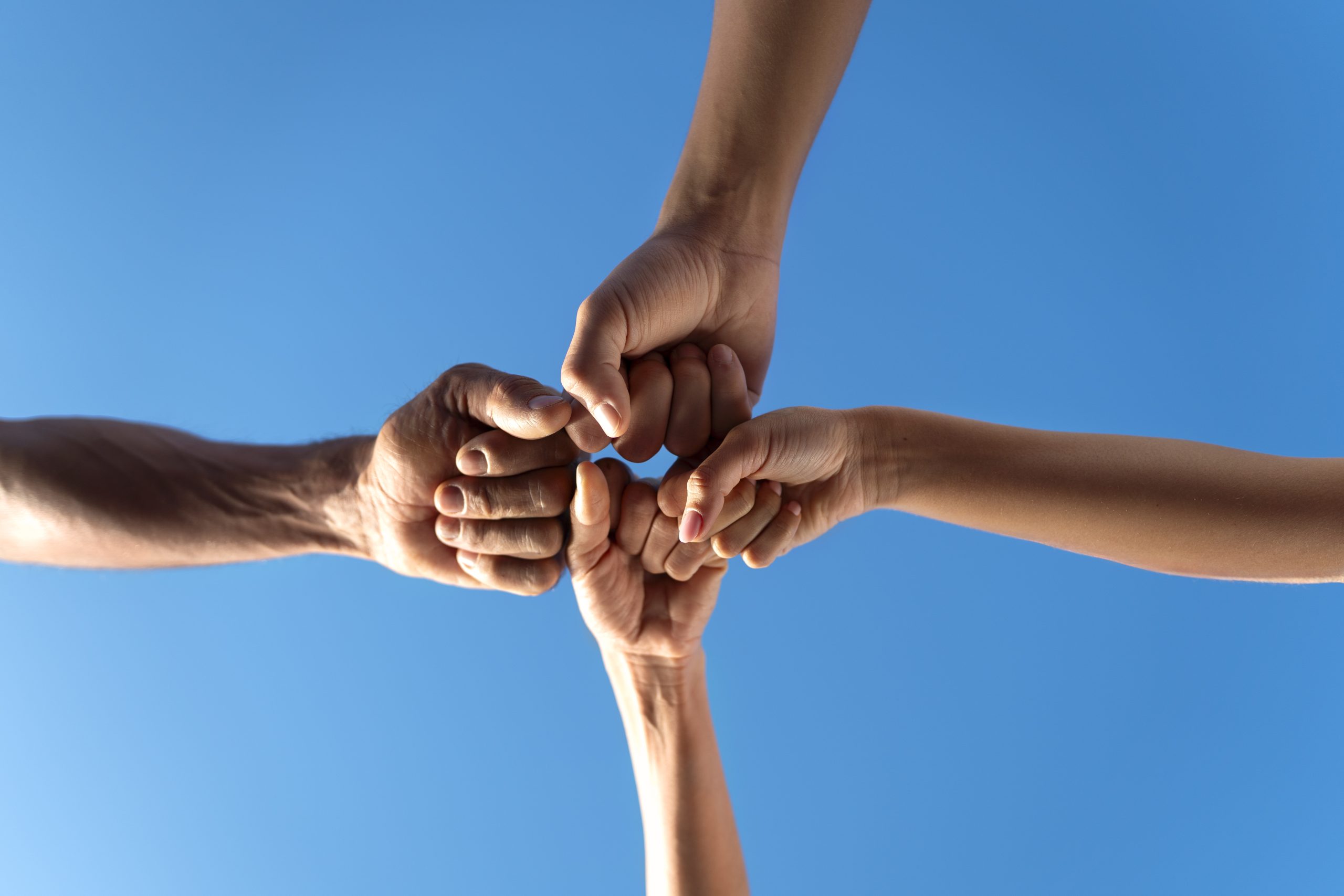 group people putting their hands together while exercising outdoors